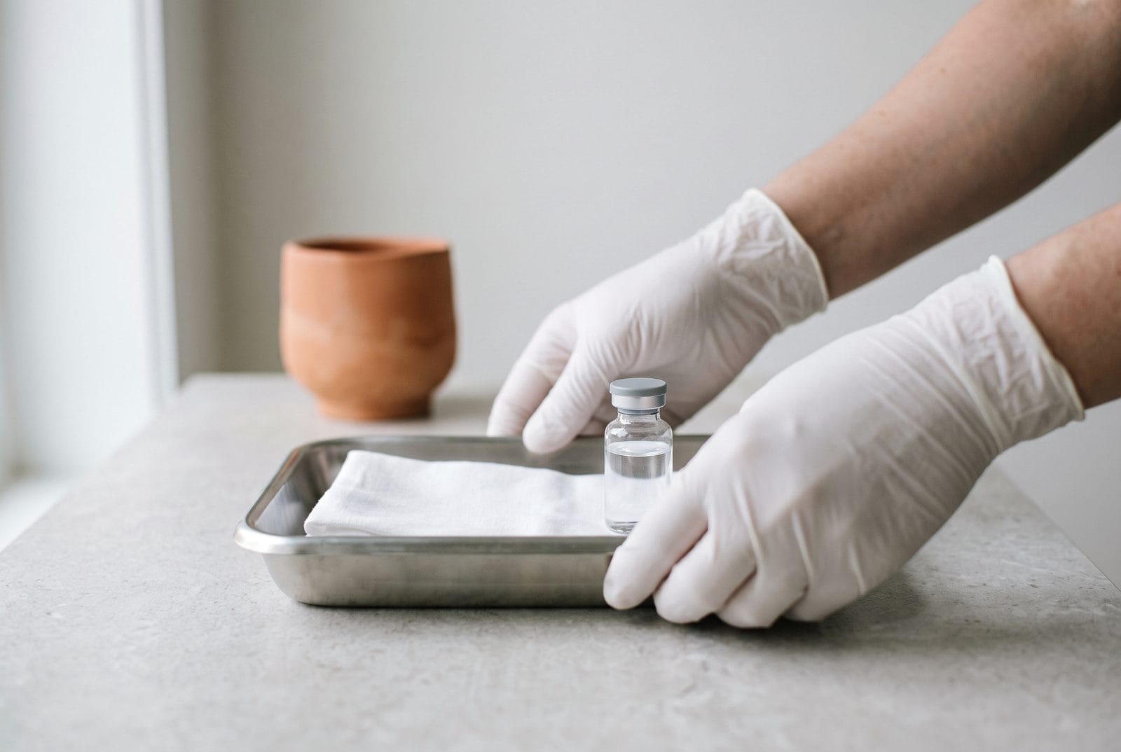Gloved hands setting a shallow stainless tray down on a pale counter, framed below the shoulder.